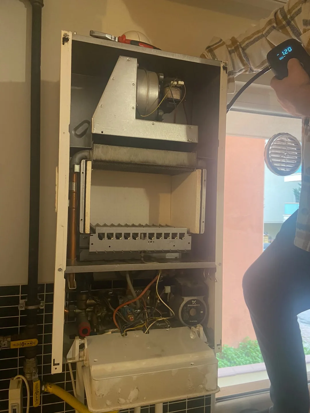 Ön kapağı açık kombi başında ölçüm ekipmanıyla çalışan teknisyen